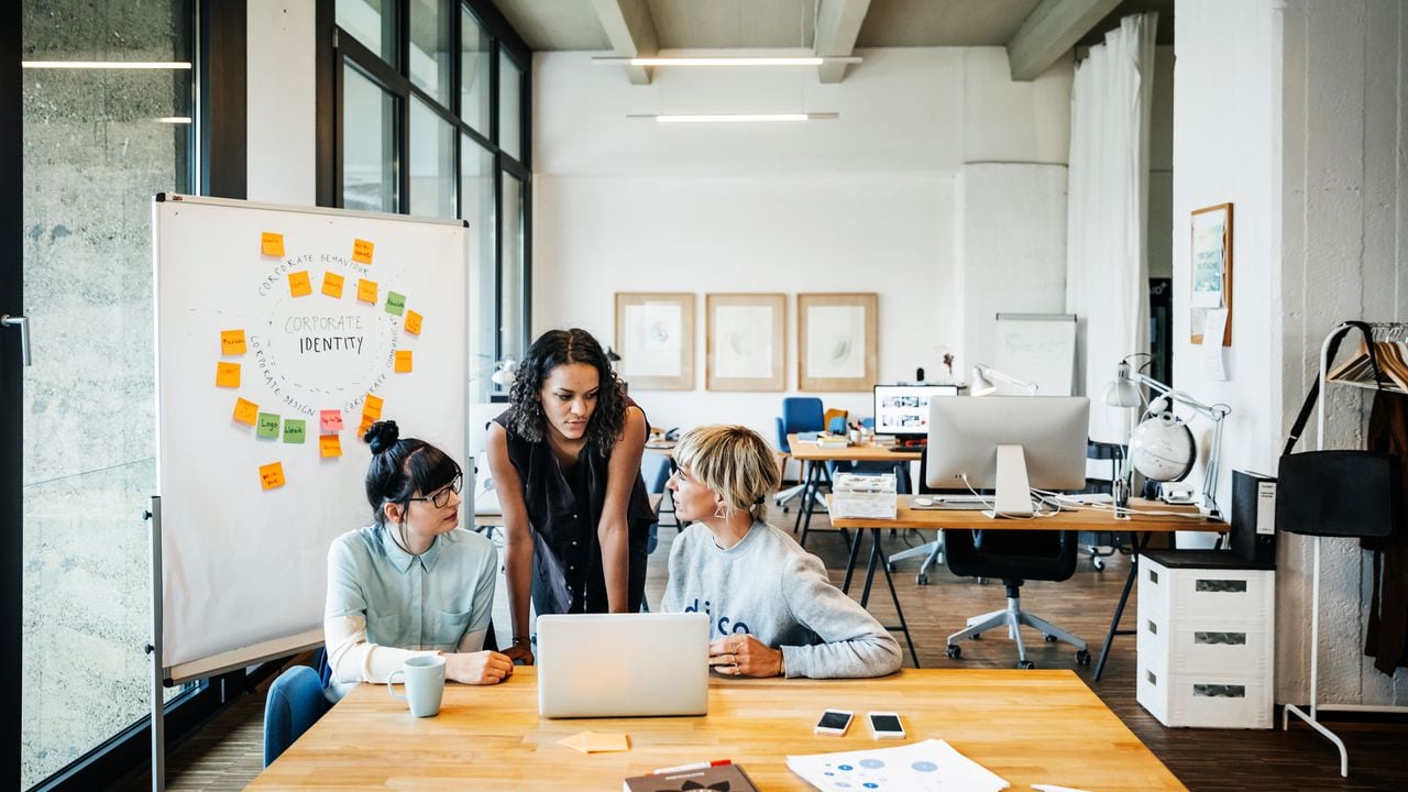 Tres mujeres empresarias jóvenes casuales que tienen una reunión con un portátil en un loft de oficina moderno.