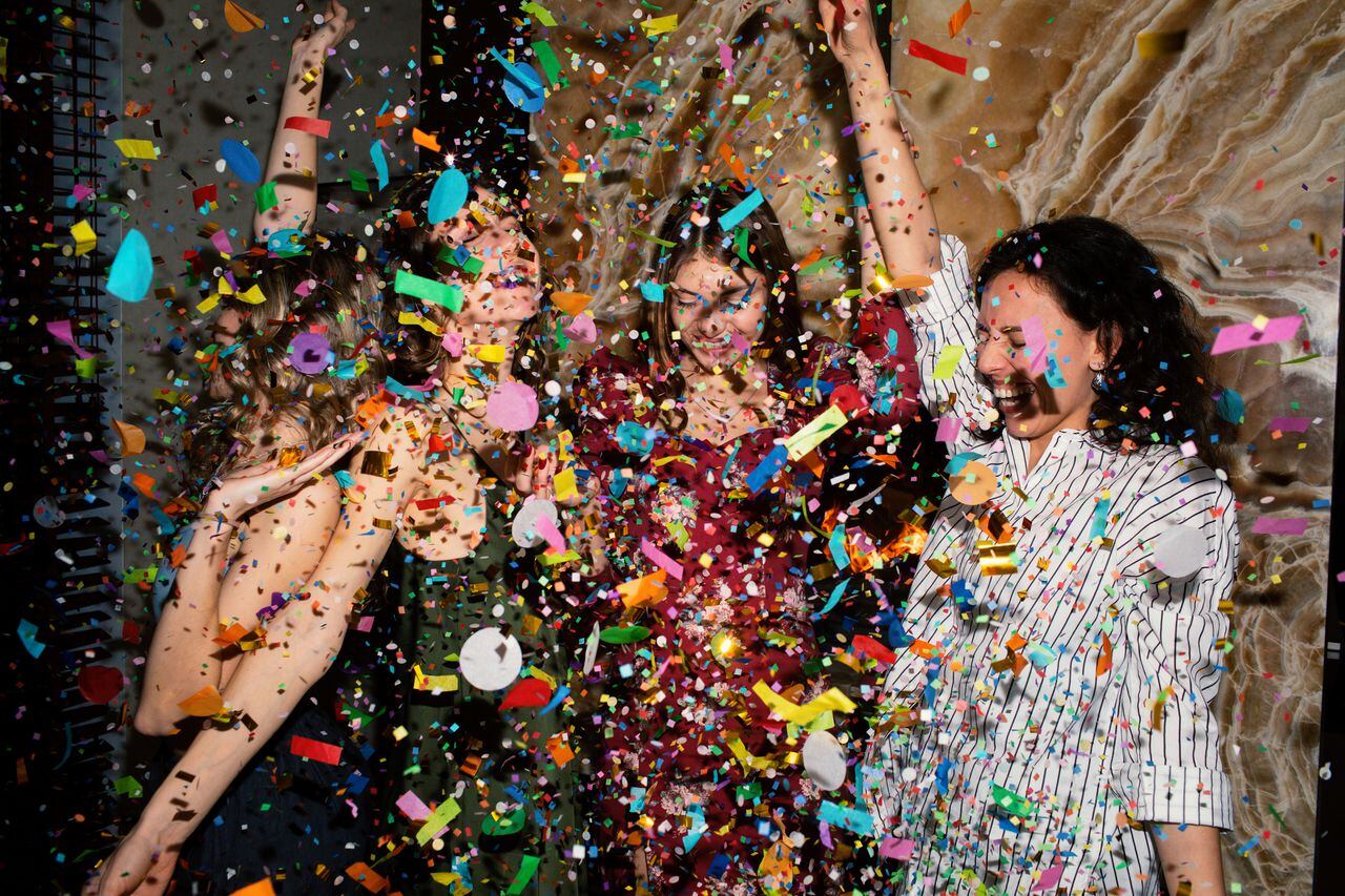 Group of beautiful young people throwing colorful confetti while dancing and looking happy. Friends making big party in the night. New year's or Birthday party. Series.