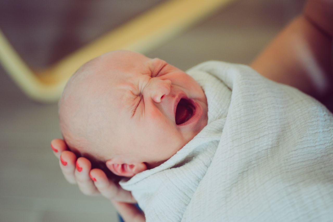 Adorable recién nacido abre la boca para bostezar o llorar, siendo sostenido por mamá y envuelto en una acogedora manta. Estilo de vida para niños, bebés, recién nacidos y padres
