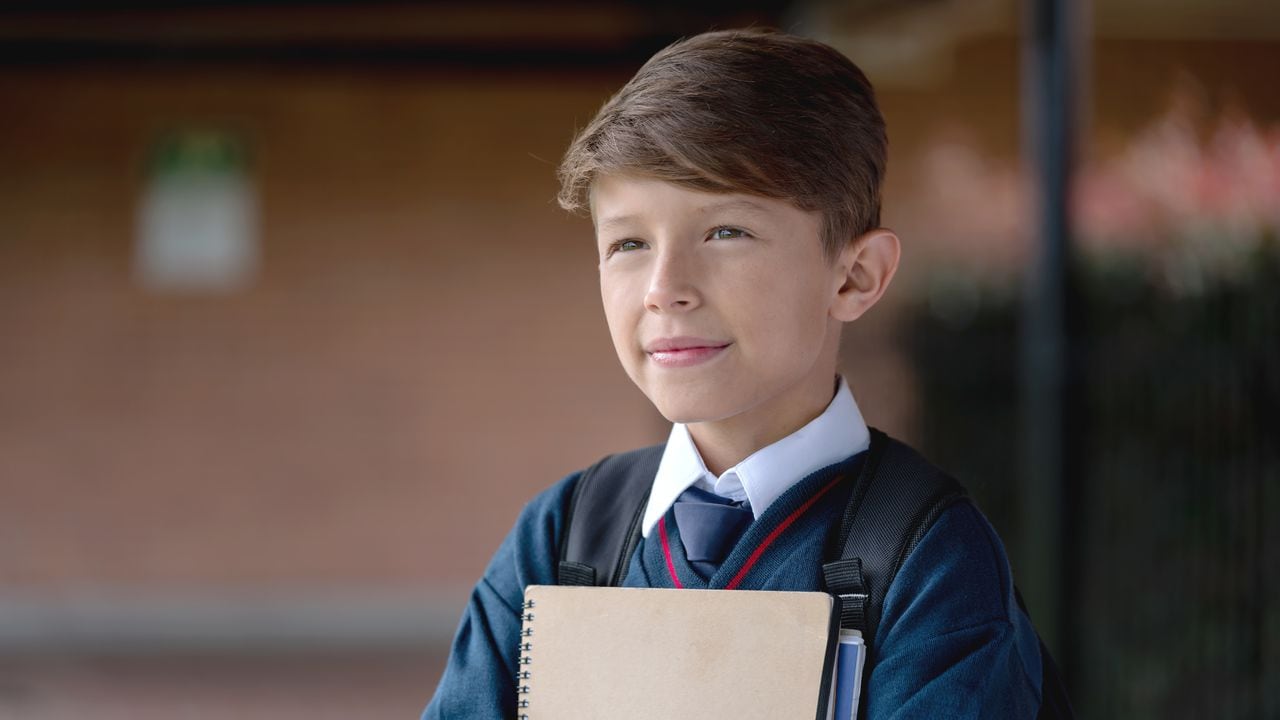 Retrato de un estudiante reflexivo en la escuela vistiendo su uniforme mientras sostiene un cuaderno