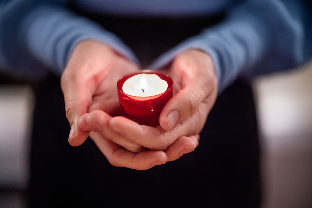 Close-up of woman holding a votive candle. Female worshipper praying with a candle in church.