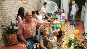 Felices padres mexicanos sentados con su nieto en sillas y jugando con un globo durante una celebración de cumpleaños en casa.