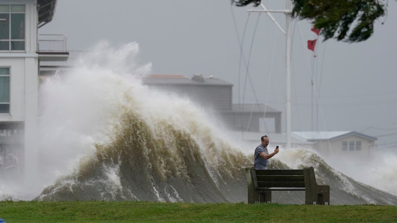 Esta fotografía muestra a un hombre que toma fotografías frente a grandes olas en la orilla del lago Pontchartrain, en Nueva Orleans, el domingo 29 de agosto de 2021. (AP Foto/Gerald Herbert)