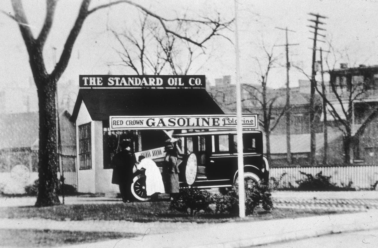 circa 1918:  Three people look under the hood of an automobile in front of a Standard Oil gas station.  (Photo by Hulton Archive/Getty Images)