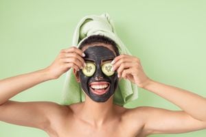 Happy smiling girl applying facial carbon mask portrait - Young woman having skin care cleanser spa day - Healthy beauty clean treatment and and self care lifestyle concept - Green background