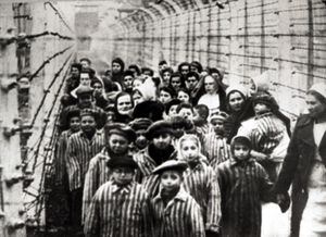 Jewish children, survivors of Auschwitz, with a nurse behind a barbed wire fence, Poland, February 1945. Photo taken by a Russian photographer during the making of a film about the liberation of the camp. The children were dressed up by the Russians with clothing from adult prisoners. (Photo by Galerie Bilderwelt/Getty Images)