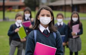 Portrait of a happy girl with a group of students at the school wearing facemasks during the COVID-19 pandemic - education concepts
