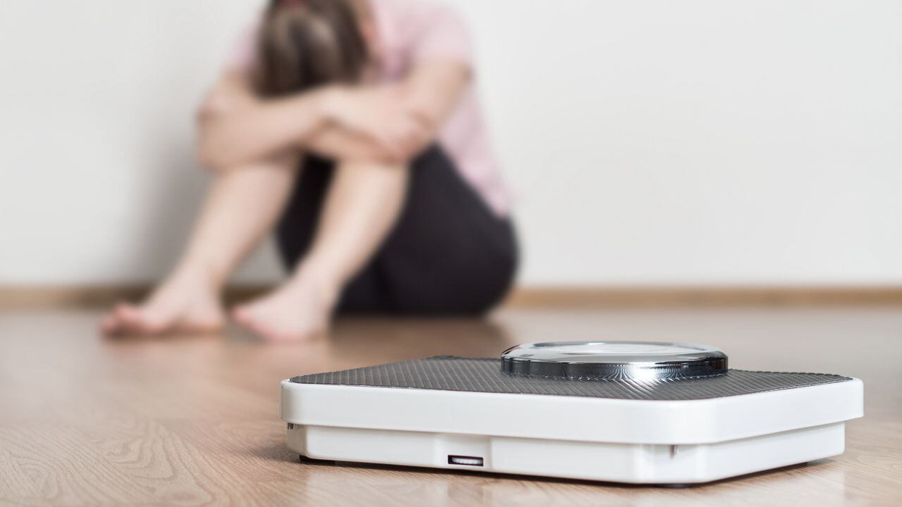 Weight loss fail concept. Scale and depressed, frustrated and sad woman sitting on floor holding head and arms on knees.