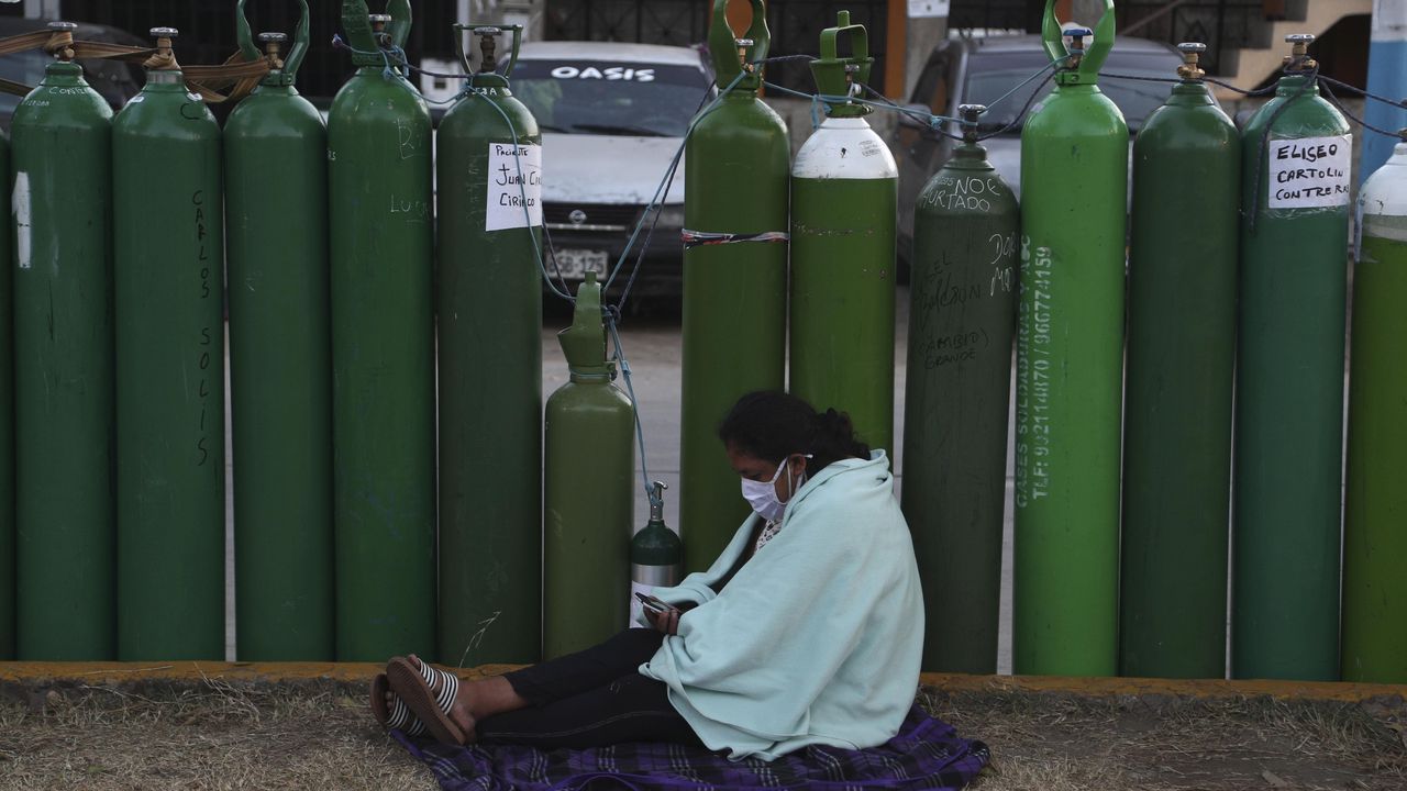 Una mujer revisa su teléfono celular mientras se sienta junto a su tanque de oxígeno vacío después de acampar durante la noche para esperar con otros a que abra una tienda de recargas en Callao, Perú. (AP Foto/Martín Mejía)