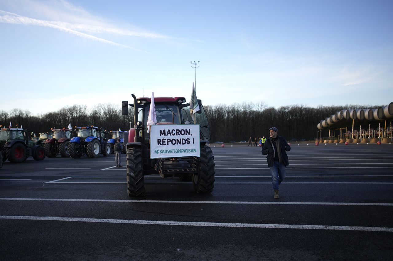 Un agricultor pasa junto a un tractor con un cartel que dice "Macron, responde", mientras los agricultores bloquean el peaje de la autopista Saint-Arnoult con sus tractores, el viernes 26 de enero de 2024 en Saint-Arnoult, al sur de París.