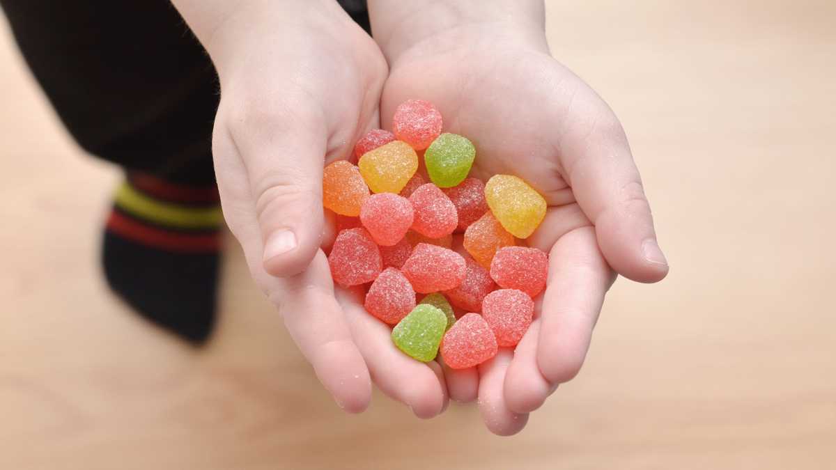 Close up of a young boy holding candy gum drops in his hands.