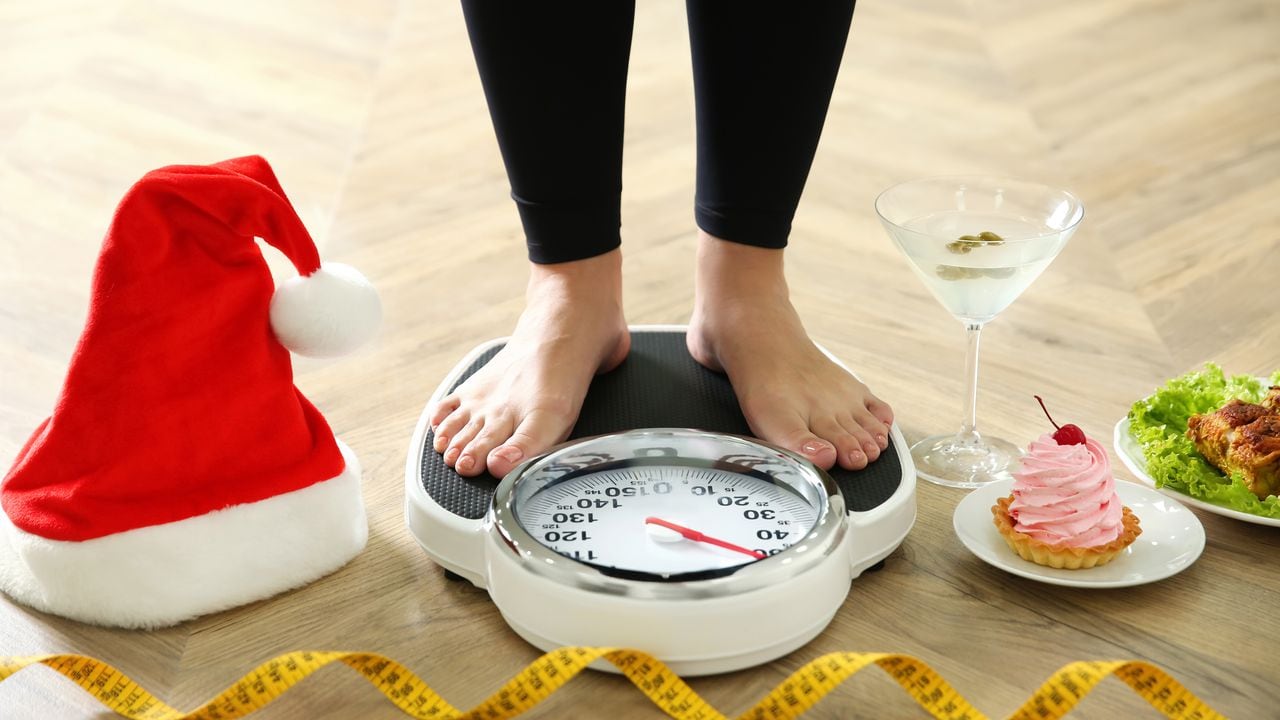 Food, alcohol left after Christmas holidays and woman with measuring tape standing on scales indoors, closeup. Overweight problem