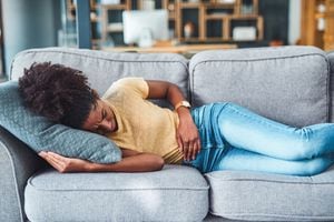 Shot of a young woman experiencing stomach pain while lying on the sofa at home