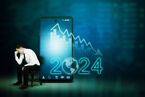 Stressed businessman sitting next to mobile phone with downtrend chart and number 2024