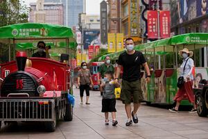 Personas que usan mascarillas para ayudar a frenar la propagación del coronavirus caminan en trenes de juguete a lo largo de una calle comercial en Shanghai, China, el lunes 23 de agosto de 2021 (AP Photo / Andy Wong).
