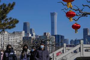 People wearing face masks to help protect from the coronavirus walk by lantern decorations for the upcoming Lunar New Year in a park seen against the city skyline in Beijing, Thursday, Jan. 27, 2022. (AP Photo/Andy Wong)