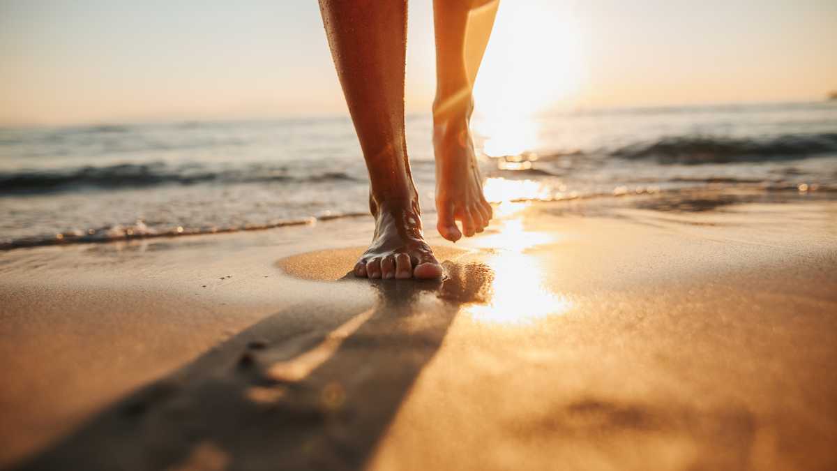 Close-up of female legs getting out of the sea water and walking on sandy beach at beautiful sunset