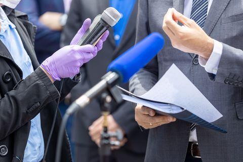 Reportero con guantes protectores y mascarilla contra la enfermedad del coronavirus COVID-19 sosteniendo el micrófono en una conferencia de prensa durante la pandemia del virus.