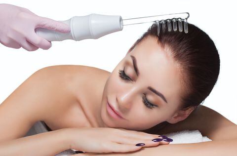 El médico-cosmetólogo realiza el procedimiento Terapia de microcorriente En el cabello de una bella y joven mujer en un salón de belleza.Cosmetología y cuidado profesional de la piel.
