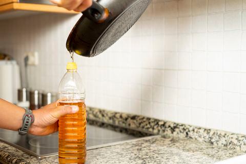 Close up of a man's hands recycling edible oil from a frying pan into a plastic bottle in his home kitchen.