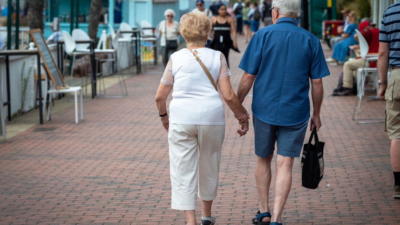 Una pareja de ancianos se dan la mano mientras caminan por el paseo marítimo de Eastbourne en East Sussex, Reino Unido.