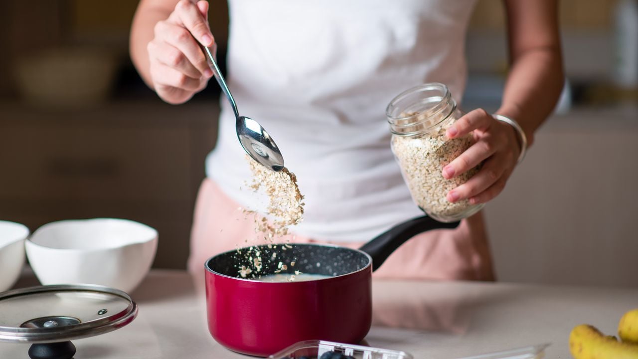 Woman making morning breakfast oatmeal cereals and adding ingredients in the kitchen at home. Making healthy organic meal packed with fiber and nutrients