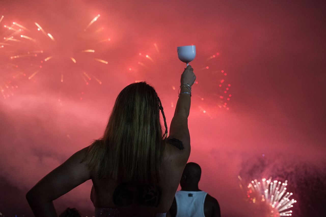 La gente celebra mientras los tradicionales fuegos artificiales de Año Nuevo iluminan el cielo en la playa de Copacabana.