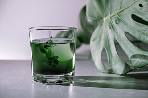 El extracto de clorofila se vierte en agua pura en un vaso sobre un fondo gris blanco con hojas verdes. Clorofila líquida en un vaso de agua. Concepto de superalimento, alimentación saludable, desintoxicación y dieta. Cámara lenta, primer plano, espacio de copia