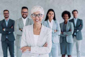 Portrait of beautiful smiling businesswoman with her colleagues. Multi-ethnic group of business persons standing together in modern office. Successful team leader and her team in background.