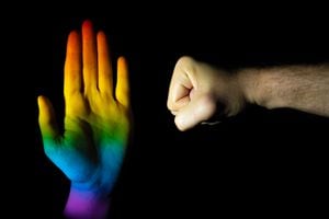 A closeup of hands making a stop and punch gesture on a black background - stopping homophobia, aggression concept