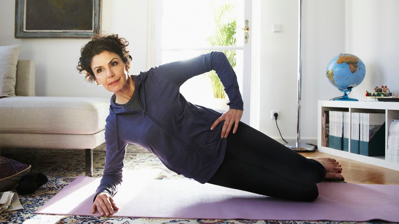 Mujer adulta media haciendo yoga en casa
