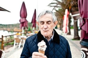 Elderly man eating an ice cream cone on a beach walkway during winter.