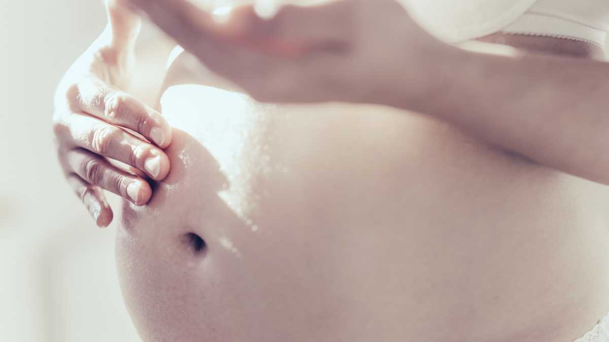 Pregnant woman rubbing oil on her belly, close up.