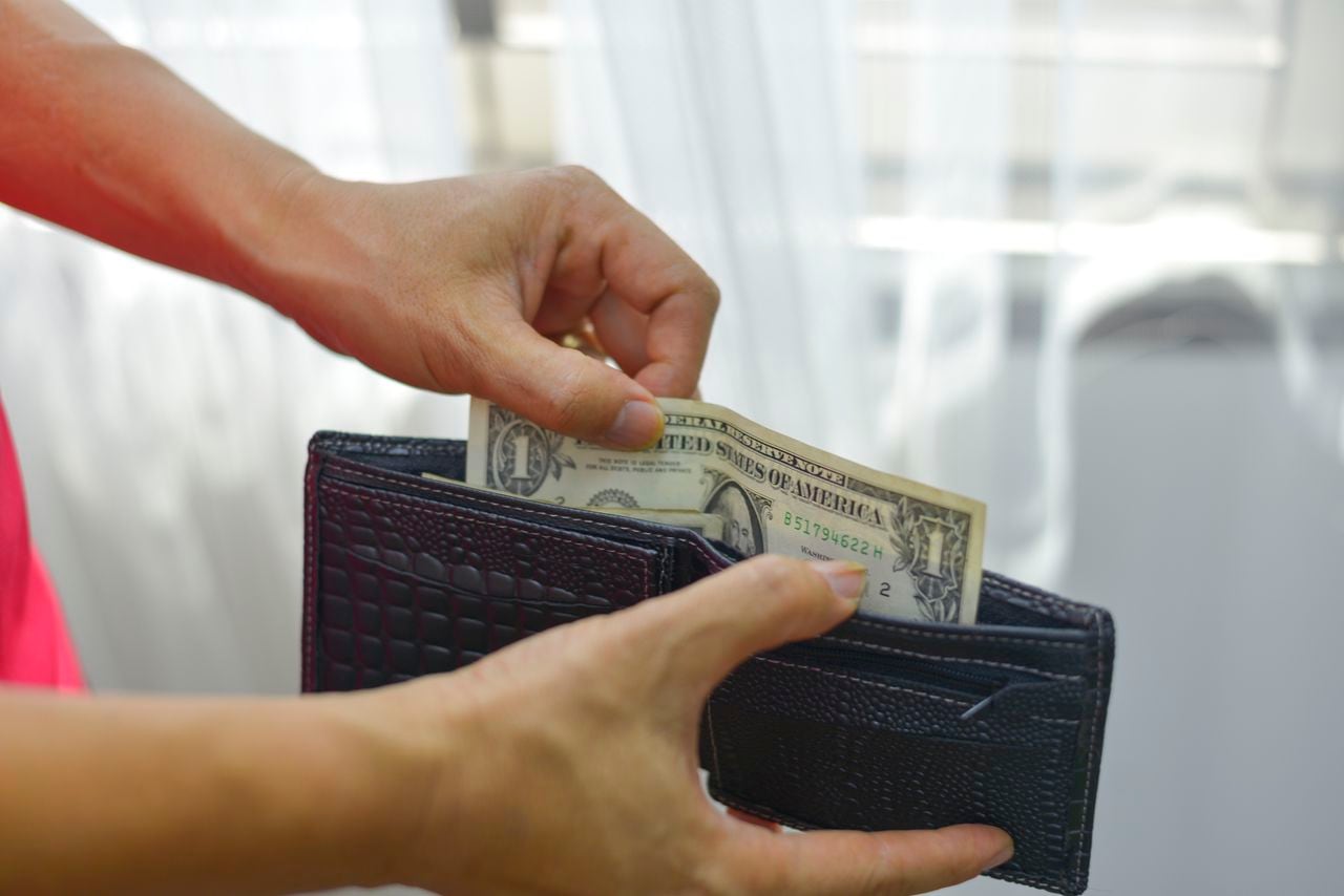 The young man is opening his wallet to pick up money from his wallet.