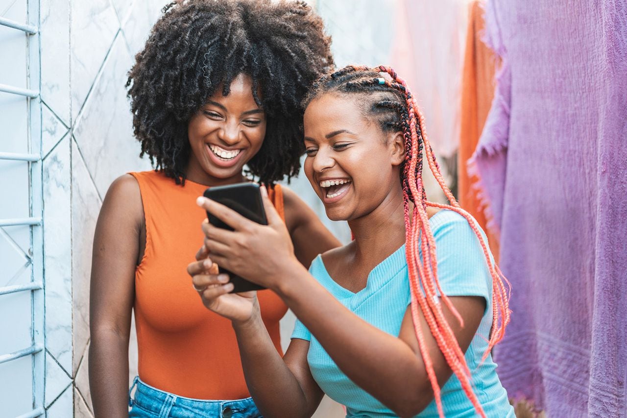 Mujeres miran celular, mujeres negras, afro, mujeres se rien viendo celular.