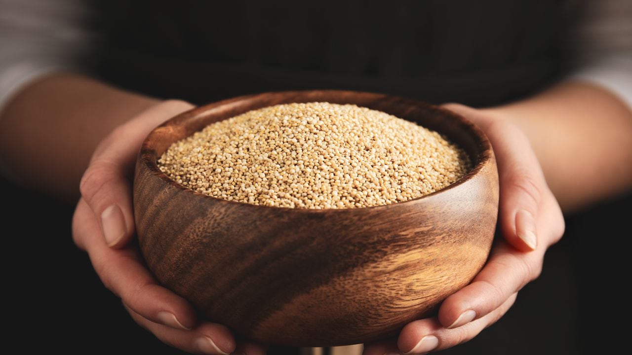 Woman holding wooden bowl with white quinoa on dark background, closeup
