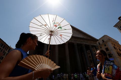 Una mujer se protege del sol bajo una sombrilla y usa un abanico plegable cerca del Panteón durante una ola de calor en Italia, en Roma