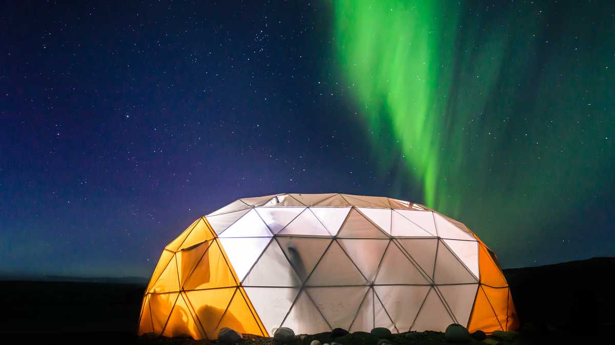 Carpa domo iluminada con aurora boreal en el fondo, en Narsaq Vestgronland, un lugar ubicado en Groenlandia