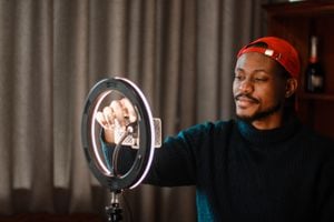 Influencer from South Africa vlogging while self-isolating. He is wearing a red cap. He is using a ring-light and a smartphone.