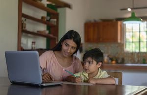 Feliz madre latinoamericana supervisando a su hijo mientras estudia en línea desde casa usando una computadora portátil - educación en el hogar durante los conceptos pandémicos