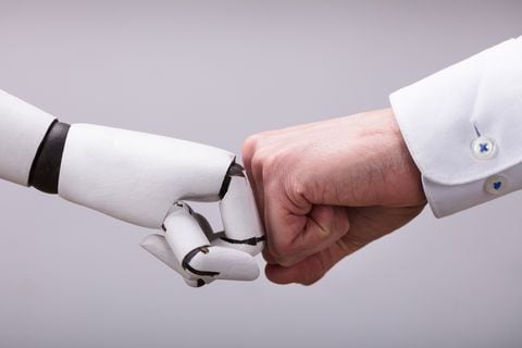 Robot y mano humana haciendo golpe de puño sobre fondo gris - Imagen de referencia