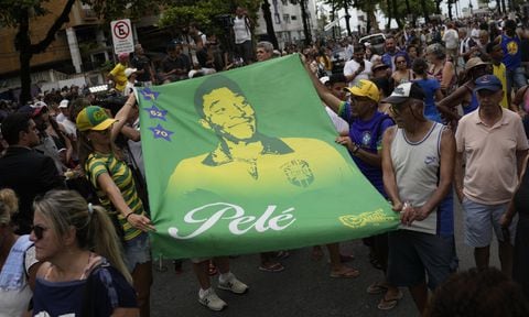 People hold a banner of the late Brazilian soccer great Pele along the route of his funeral procession from Vila Belmiro stadium to the cemetery in Santos, Brazil, Tuesday, Jan. 3, 2023. (AP/Matias Delacroix)