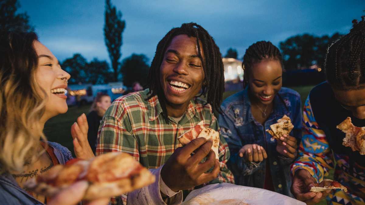 A young group of friends laughing and sharing pizza at a music festival.