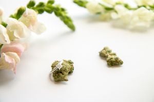 A diamond engagement ring sits atop a marijuana bud, surrounded by flowers.