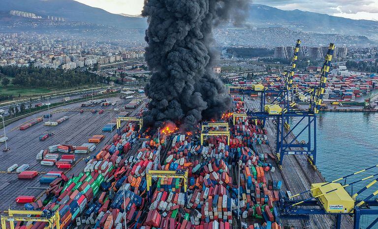 This handout photograph taken and released by Turkish agency DHA (Demiroren News Agency) shows smoke rising from burning containers at the harbor of Iskenderun in Hatay, a day after a 7.8-magnitude earthquake struck the country's southeast, on February 7, 2023. - Rescuers in Turkey and Syria braved frigid weather, aftershocks and collapsing buildings, as they dug for survivors buried by an earthquake that killed more than 5,000 people. Some of the heaviest devastation occurred near the quake's epicentre between Kahramanmaras and Gaziantep, a city of two million where entire blocks now lie in ruins under gathering snow. (Photo by Handout / DHA (Demiroren News Agency) / AFP) / - Turkey OUT / RESTRICTED TO EDITORIAL USE - MANDATORY CREDIT "AFP PHOTO /  DHA (Demiroren News Agency) " - NO MARKETING NO ADVERTISING CAMPAIGNS - DISTRIBUTED AS A SERVICE TO CLIENTS