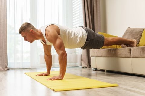 Hombre musculoso haciendo flexiones durante el entrenamiento en casa. Músculos, masa muscular, ejercicio físico, tonificar.