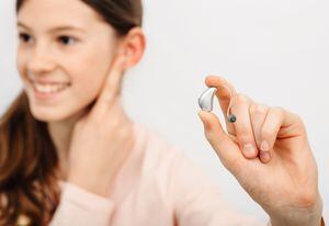 Solución auditiva para niños. Niña sosteniendo un audífono, tratamiento de la sordera en niños. Audiología
