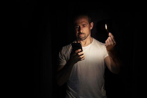 Hombre mira que su teléfono no tiene batería, mientras no hay luz en su casa.