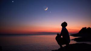 Silueta de un hombre mirando la luna y las estrellas sobre el horizonte del océano.