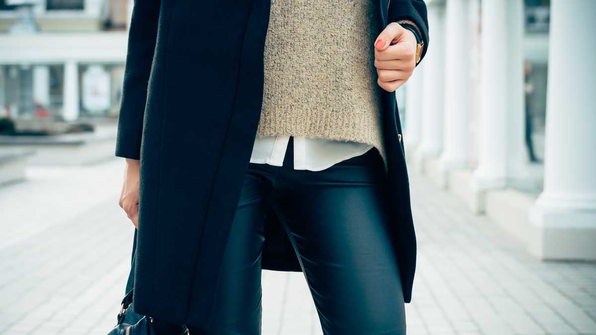 Details of women's clothing. Close-up of a woman in a sweater, coat, black pants. In her hand female bag.